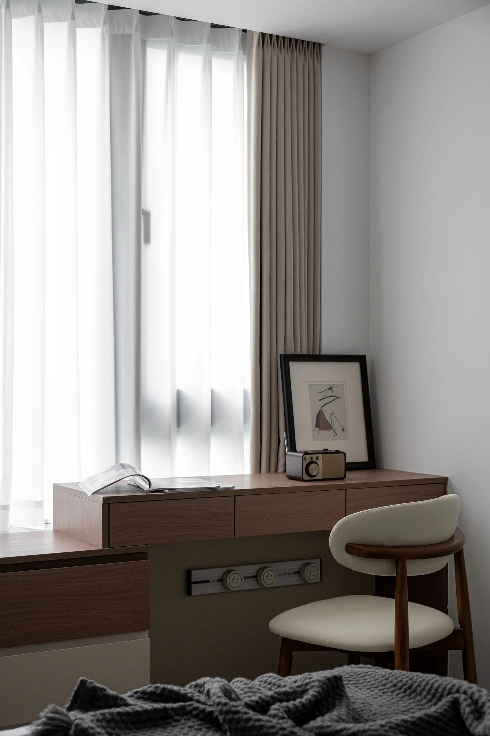 Escritorio de madera junto a una ventana con cortinas claras, acompañado por una silla tapizada.