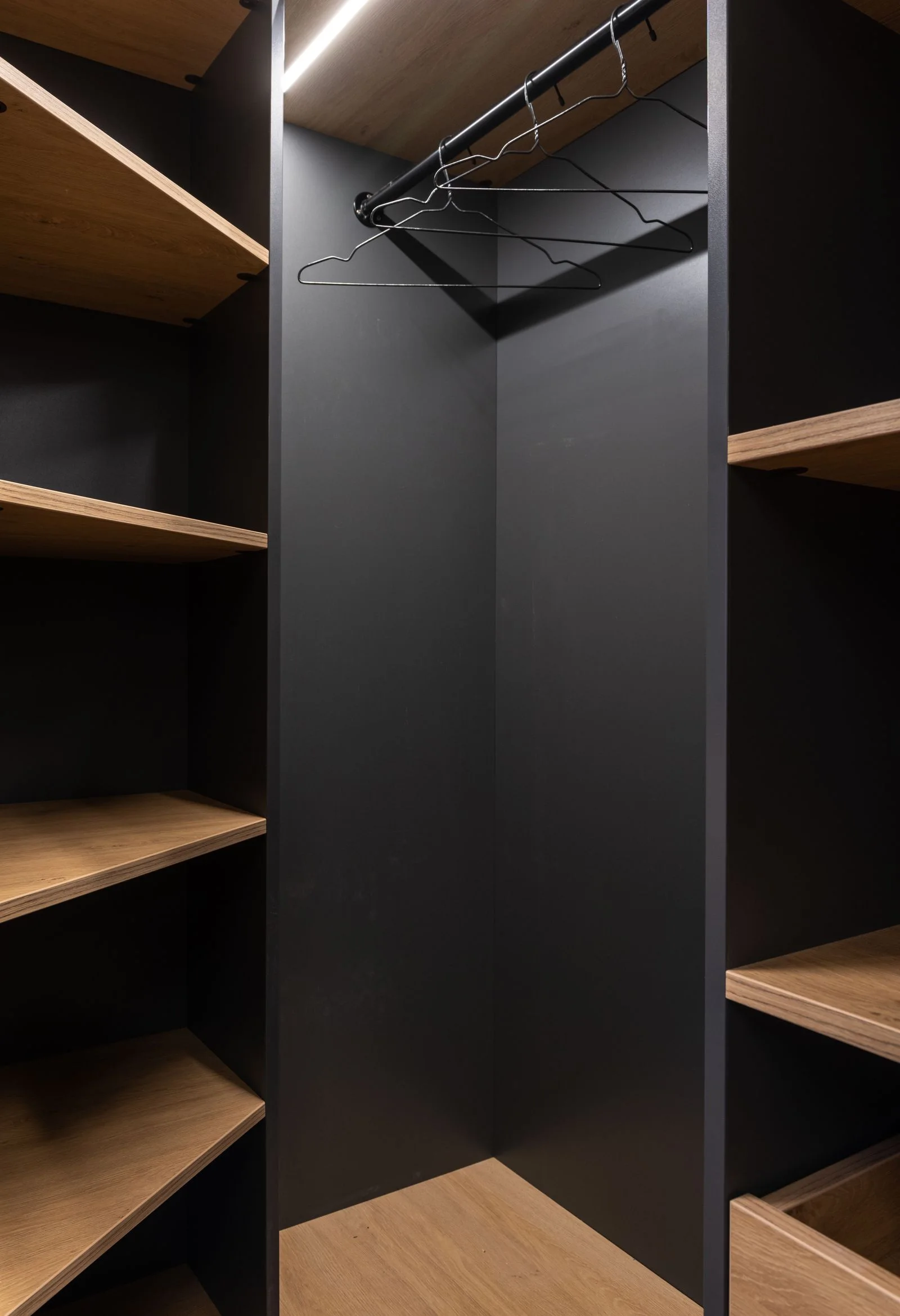 Interior de un placard con estantes de madera y barral sobre un fondo oscuro.